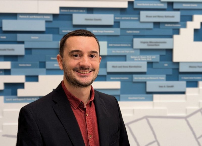 Alberto Cano, associate vice president for research computing, smiling in front of a blue donor-recognition wall.