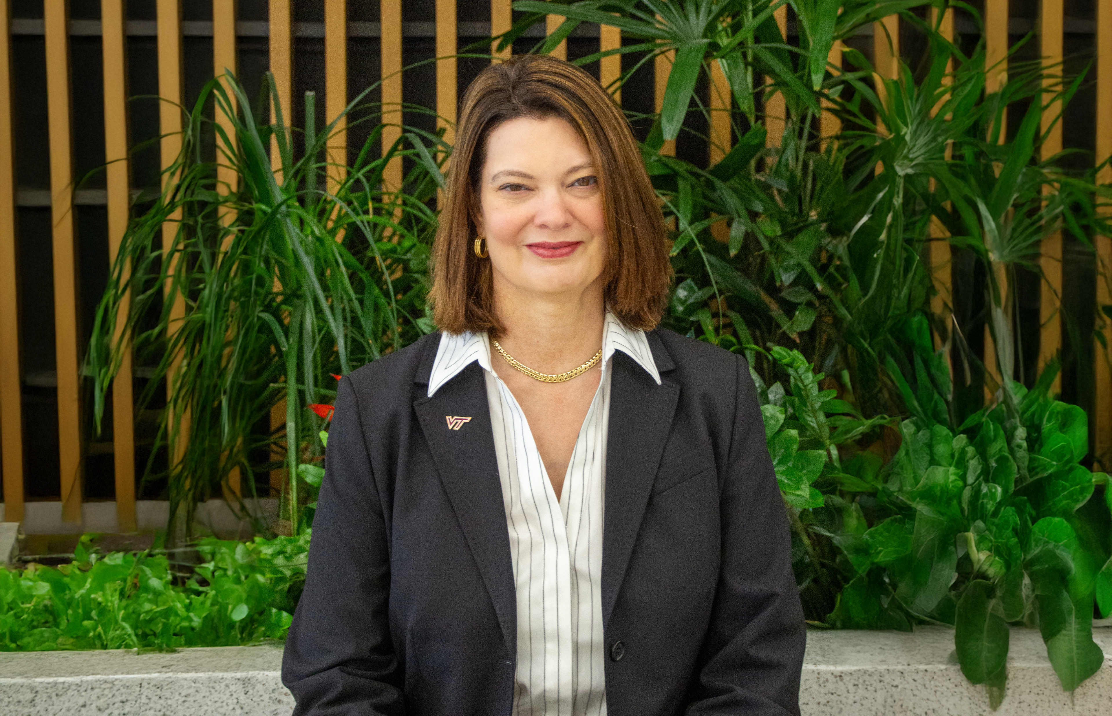 Portrait of Sharon P. Pitt, Vice President for Information Technology and Chief Information Officer at Virginia Tech, smiling and wearing a dark blazer with a VT pin, standing in front of indoor greenery.