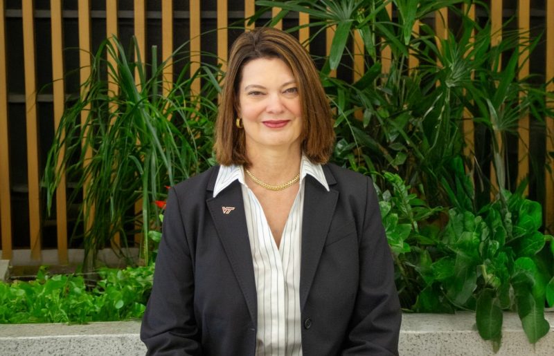 Portrait of Sharon P. Pitt, Vice President for Information Technology and Chief Information Officer at Virginia Tech, smiling and wearing a dark blazer with a VT pin, standing in front of indoor greenery.