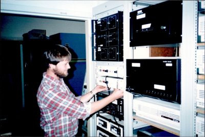 Brian Jones, ca. 1984, works on the LocalNet Headend in the old Burruss Hall switch room. Tellabs phone echo cancellation gear is visible in the bottom right corner.