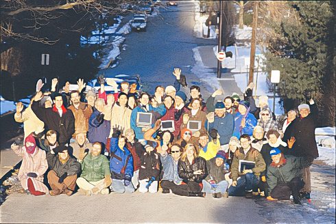 A group picture of users and members of the Blacksburg Electronic Village standing in a street in Blacksburg Virginia in winter. Some are holding computers. 
