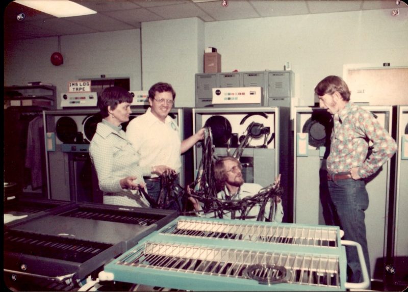 people standing next to a computer holding a bunch of magnetic tape