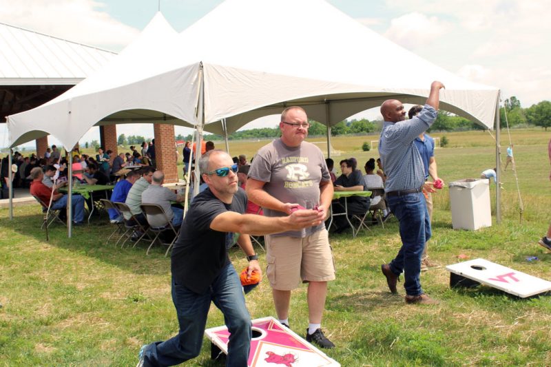 three coworkers tossing cornhole at company picnic