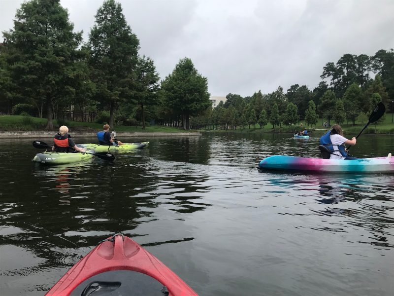 Group of people kayak on a calm lake on a cloudy summer day